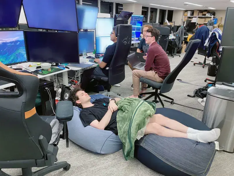 Sam Bankman-Fried dort sur des fauteuils gonflables dans le bureau de FTX à Hong Kong, tandis que des employés travaillent à leurs postes en arrière-plan.