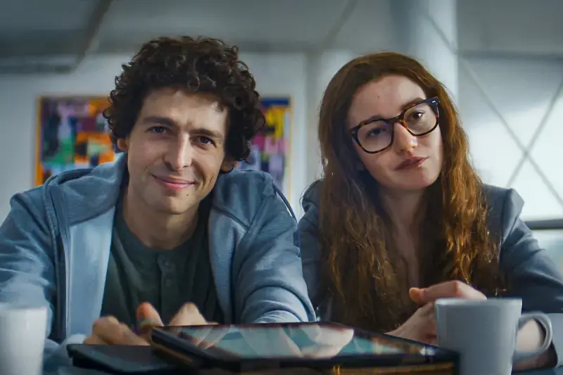 Sam Bankman-Fried (interprété par Anthony Boyle) et Caroline Ellison (interprétée par Julia Garner) assis ensemble à une table.